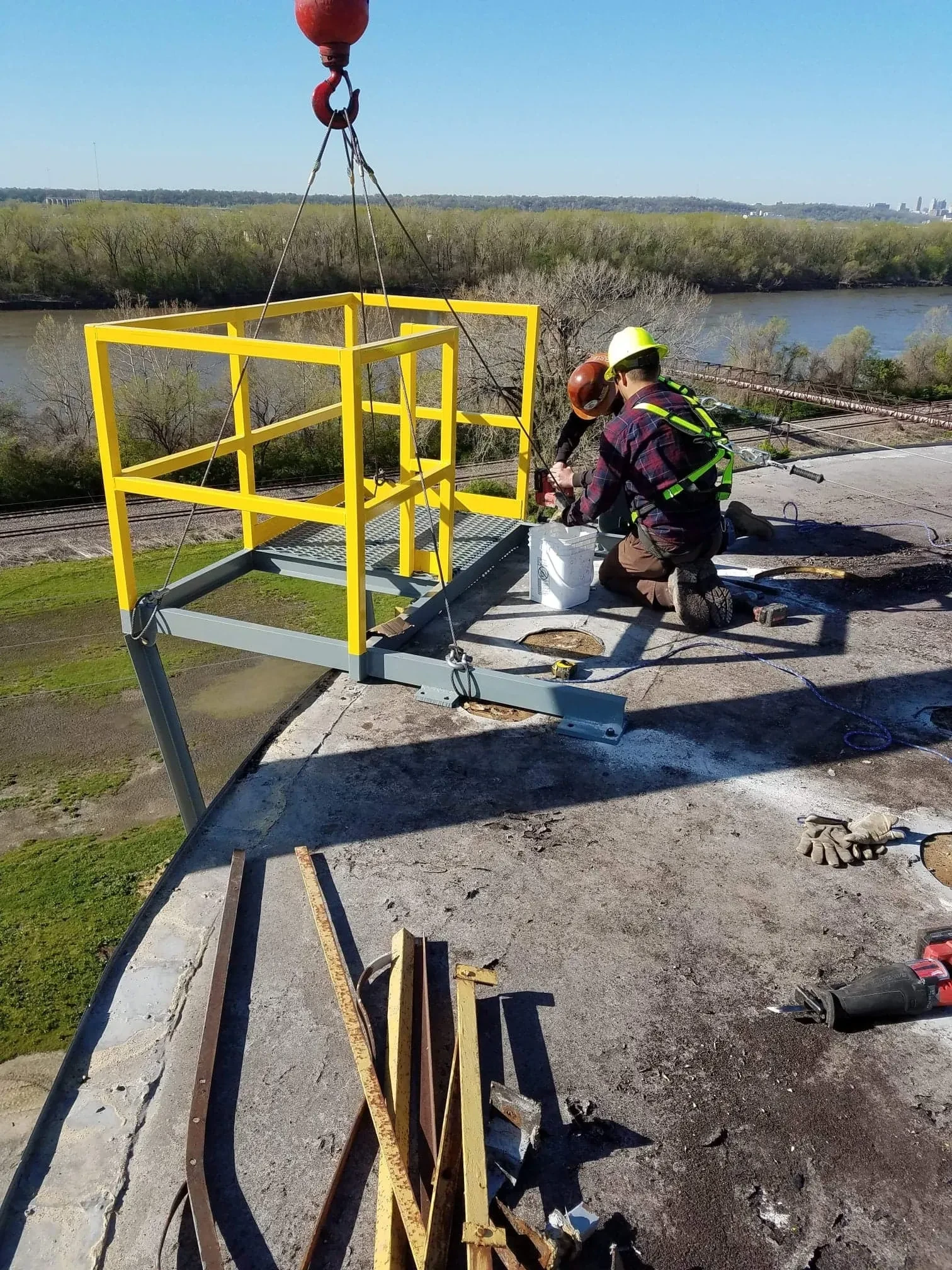 Workers installing yellow steel safety cage lifted by crane